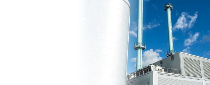 Vista exterior de una planta de cogeneración industrial con grandes tanques blancos y dos chimeneas azules.