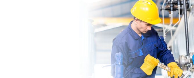Técnico industrial con casco amarillo y guantes de seguridad, realizando un ajuste en una planta de cogeneración con una llave inglesa.