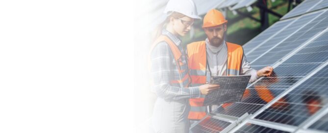 Dos ingenieros o técnicos, hombre y mujer, con cascos y chalecos de seguridad, revisando planos de una instalación de paneles solares industriales.